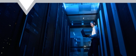 Server technician working with laptop in walkway of data facility